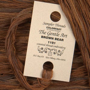 May include: A brown embroidery floss skein with a label that reads "Sampler Threads Colorfast by industry standards The Gentle Art BROWN BEAR 1191 counted thread embroidery P.O. Box 670 New Albany, Ohio 43054"