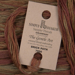 May include: A skein of Simply Shaker Sampler Threads in the color Brick Path 7086. The thread is a blend of brown, green, and red.