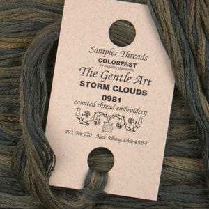 May include: A brown and green embroidery floss skein with a label that reads "Sampler Threads COLORFAST by industry standards The Gentle Art STORM CLOUDS 0981 counted thread embroidery PO Box 670 New Albany, Ohio 43054"