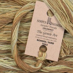 May include: A skein of "Simply Shaken" sampler threads in School Yard color, with a colorfast label. The thread is a mix of light and dark tan and olive green hues, ideal for counted thread embroidery.