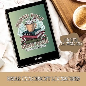 May include: A digital illustration of a Kindle e-reader with a green background and a Christmas-themed design. The design features a cup of hot chocolate with whipped cream and a candy cane, a stack of books, and the text "North Pole Book Club, Hot Cocoa Served Daily".