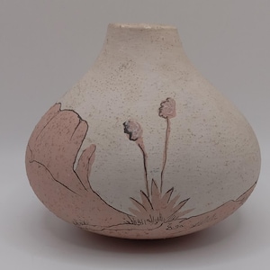 May include: A speckled, off-white ceramic vase with a rounded body and a narrow neck. The vase features a hand-painted design of pink desert flora and a landscape scene. The design includes a large pink flower and two smaller flowers.