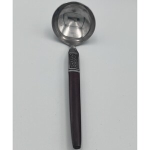 May include: A silver ladle with a dark brown wooden handle. The ladle's bowl is round and reflective. The handle has a decorative silver band near the bowl and a long, smooth, dark brown wooden grip. A kitchen utensil.