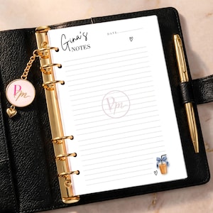 May include: A black leather binder with gold rings holding a white lined paper insert titled Gina's Notes. The page features a date line, small heart icons, a central PM logo, and a graphic of an iced coffee with a blue bow. A gold pen is attached.