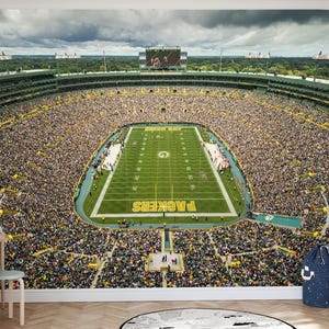 May include: An aerial view of a packed football stadium with a green field and the words "Packers" on the field. The stadium is filled with fans wearing green and yellow.