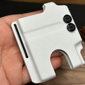 Puede incluir: Cartera de cuero blanco con una banda el&aacute;stica negra y dos tornillos negros. La cartera tiene una ranura para tarjetas y un clip para billetes.