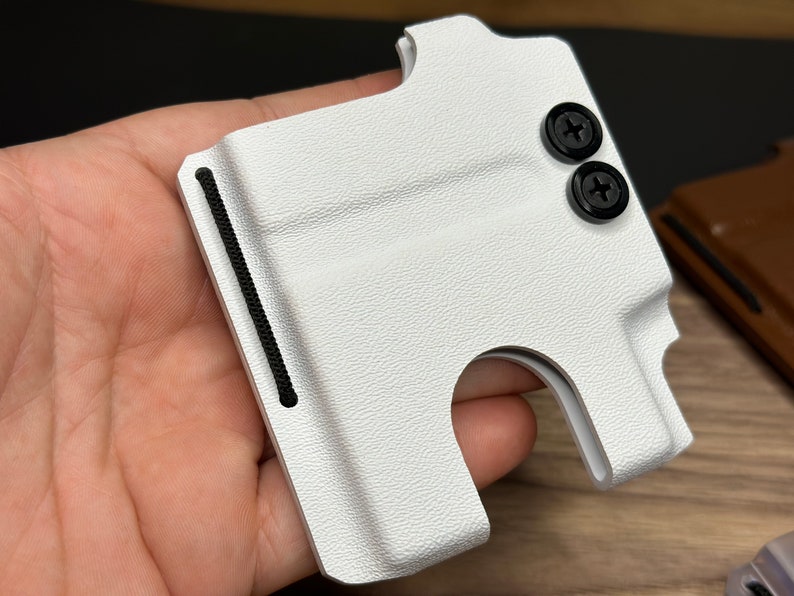 Puede incluir: Cartera de cuero blanco con una banda el&aacute;stica negra y dos tornillos negros. La cartera tiene una ranura para tarjetas y un clip para billetes.