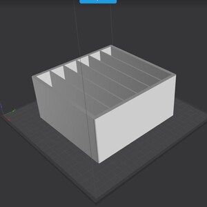 May include: A light gray rectangular organizer with five vertical dividers. The dividers are triangular at the top, creating individual compartments. The organizer sits on a dark gray surface, and is likely 3D printed.