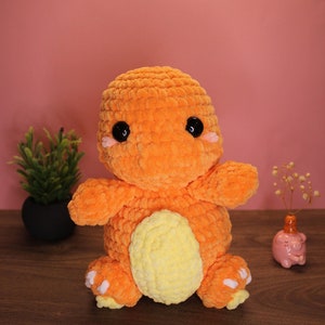 May include: Orange and yellow crocheted plush toy shaped like a dinosaur. The toy has black eyes and a friendly expression.