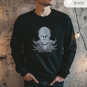May include: Black sweatshirt with a graphic print of a man's face with a grid pattern and nails on his head. The graphic is in black and white.
