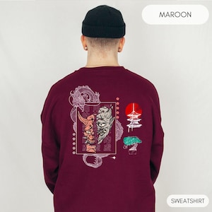 May include: Maroon sweatshirt with a white graphic print of a dragon, a Japanese temple, a bonsai tree, and two masks. The text "MAROON" is in the top right corner and "SWEATSHIRT" is in the bottom right corner.