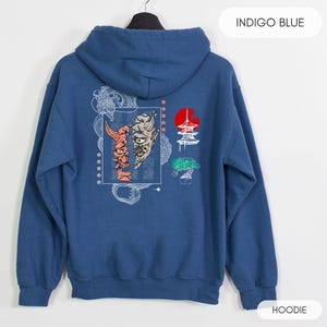 May include: Indigo blue hoodie with a graphic print of a Japanese demon mask, a pagoda, and a bonsai tree. The text "INDIGO BLUE" is printed in white at the top of the image. The word "HOODIE" is printed in white at the bottom of the image.