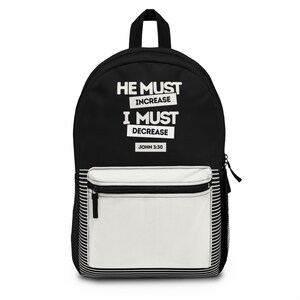 Puede incluir: Mochila negra con un bolsillo frontal blanco y el texto "HE MUST INCREASE I MUST DECREASE JOHN 3:30" en blanco. La mochila tiene una cremallera negra y un asa negra en la parte superior. El bolsillo frontal tiene un diseño a rayas blanco y negro.
