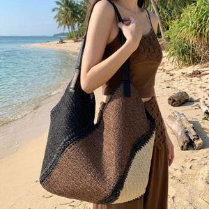 Peut inclure: Un grand sac à bandoulière de style hobo présentant un motif à chevrons tissé dans un design color-block. Le sac passe du noir à gauche au marron au centre et au crème à droite, fini avec des bretelles noires aspect cuir.