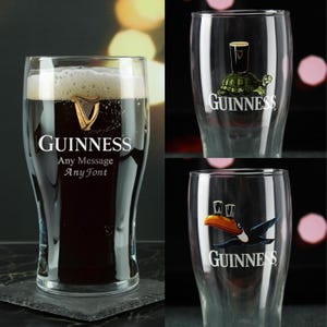 May include: Three Guinness pint glasses. One glass is filled with dark beer and foam, with the Guinness logo and text. Two other glasses have Guinness logos with a turtle and a toucan. The glasses are on a dark surface.