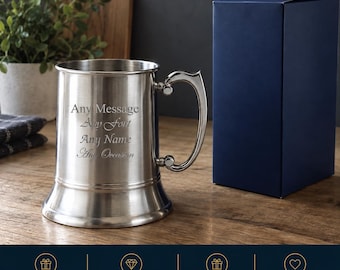 May include: A silver-toned metal tankard with a flared base and a curved handle. The front of the tankard is engraved with the text: Any Message, Any Font, Any Name, Any Occasion. A plain dark blue rectangular box stands next to the tankard.