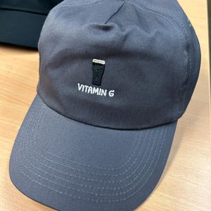 May include: A gray baseball cap with a white embroidered design of a pint glass and the text "VITAMIN G".