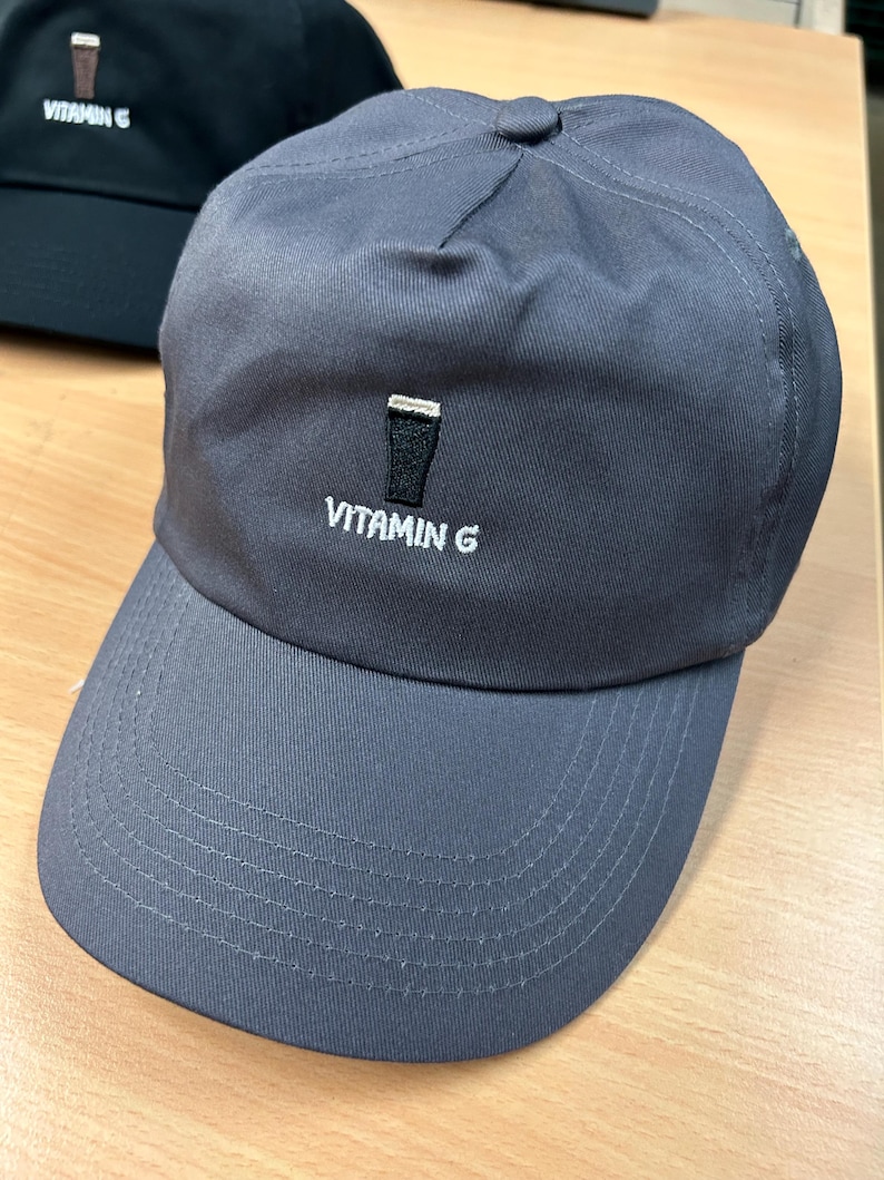 May include: A gray baseball cap with a white embroidered design of a pint glass and the text "VITAMIN G".