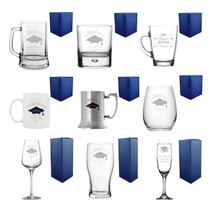 May include: An assortment of clear glass drinkware, including mugs, tumblers, and stemware, each etched with a graduation cap design and the word "Congrats". Each piece is paired with a navy blue gift box.