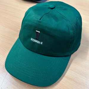 May include: A green baseball cap with a black and white embroidered image of a pint glass and the text "VITAMIN G".
