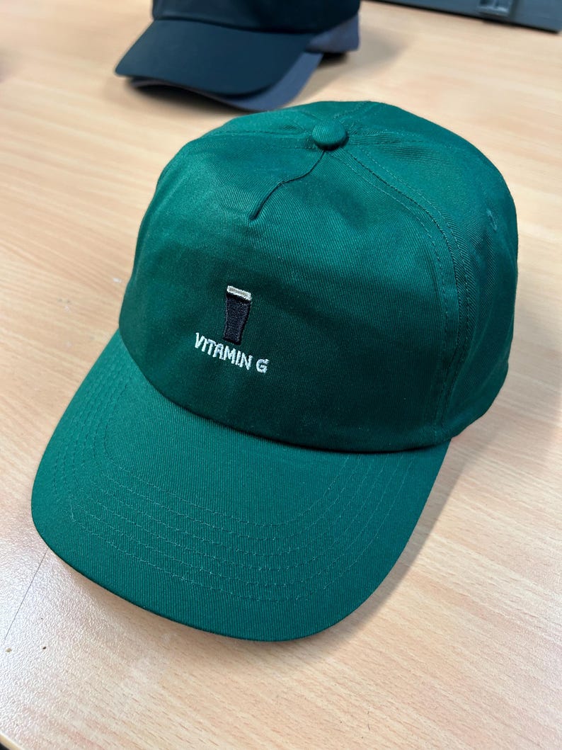 May include: A green baseball cap with a black and white embroidered image of a pint glass and the text "VITAMIN G".