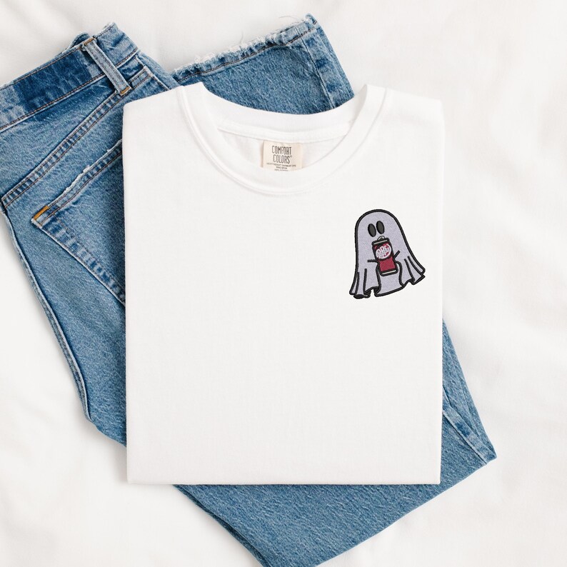 May include: White t-shirt with a ghost holding a can of soda embroidered on the front. The ghost is grey and the can is red.