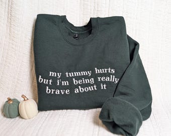 May include: A dark green sweatshirt with the text "my tummy hurts but i'm being really brave about it" in white embroidery.