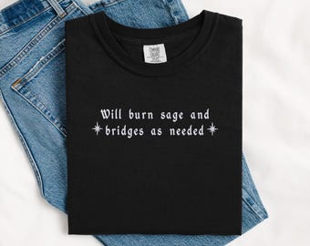 May include: Black t-shirt with white text that reads "Will burn sage and *bridges as needed*" with a star on either side of the word "bridges".