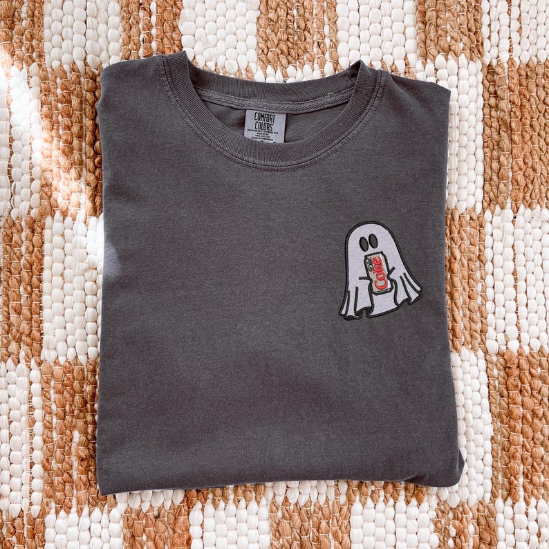 Op de afbeelding: Een antracietgrijs T-shirt met ronde hals en een kleine geborduurde afbeelding op de linkerborst. Het ontwerp toont een wit spook met zwarte omlijning dat een rood-zilveren frisdrankblikje vasthoudt met de tekst Diet Coke erop.