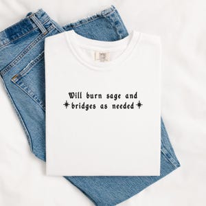 May include: White t-shirt with black text that reads "Will burn sage and *bridges as needed*"