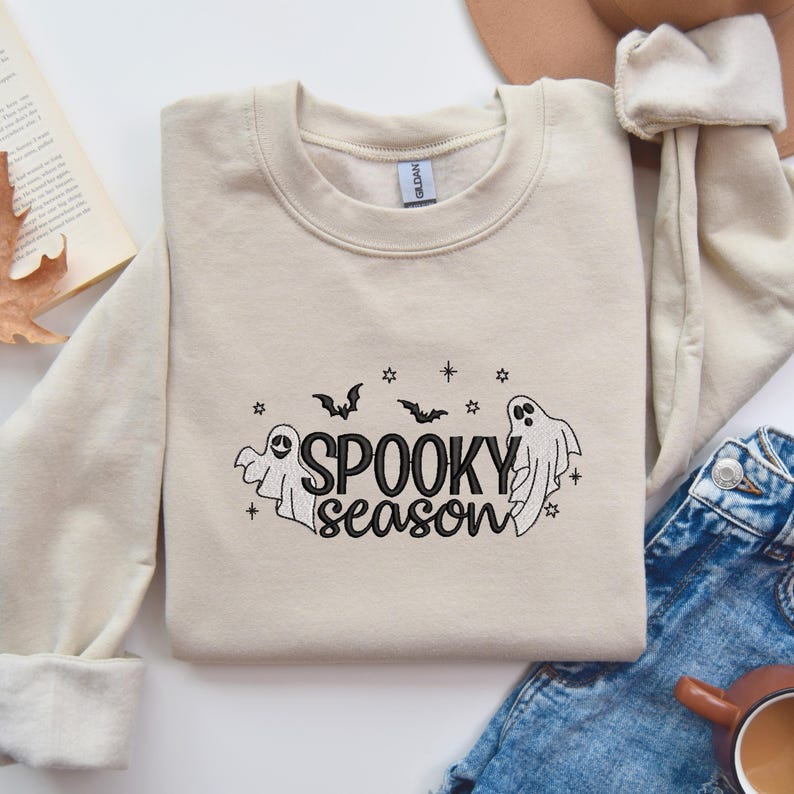 May include: A beige sweatshirt with a black embroidered design that says "Spooky Season" with two ghosts and bats.