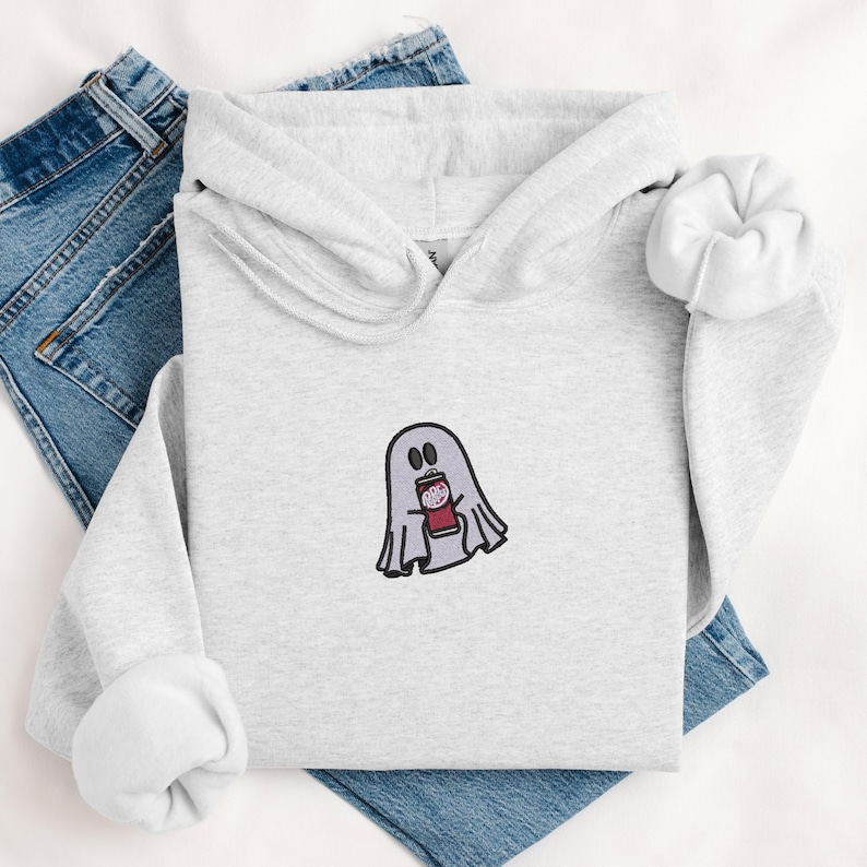 May include: A gray hoodie with a ghost holding a can of soda embroidered on the front. The ghost is white with a red mouth and black eyes.
