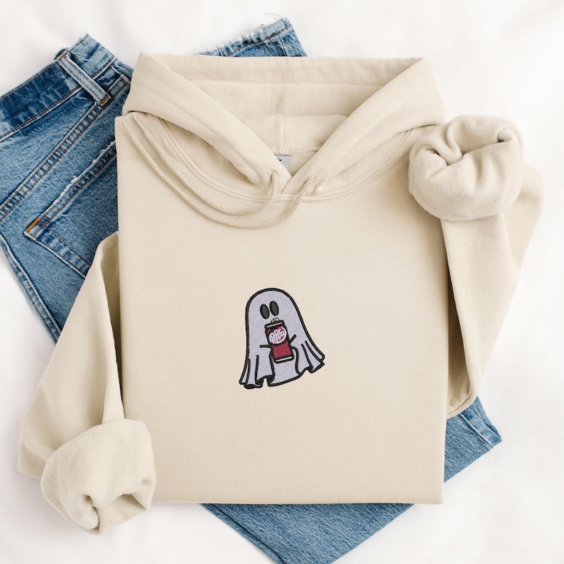 May include: A cream-colored hoodie with a ghost holding a can of soda embroidered on the front.