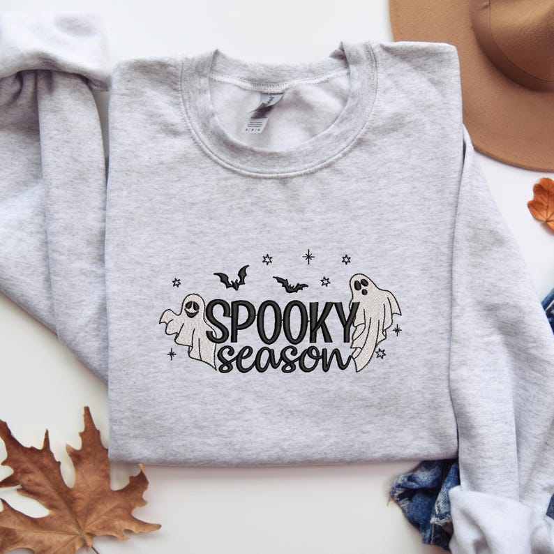 May include: A gray sweatshirt with a black embroidered design of ghosts, bats, and stars. The text "Spooky season" is embroidered in black.