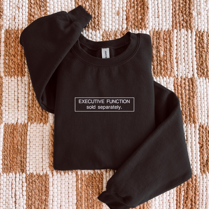 May include: A black long-sleeve crewneck sweatshirt featuring a white rectangular outline on the chest. Inside the rectangle, the text reads "EXECUTIVE FUNCTION" on the top line and "sold separately." on the bottom line in a white sans-serif font.