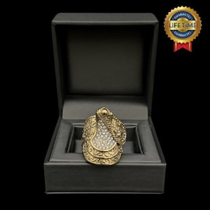 May include: A gold ring featuring a saddle design with clear rhinestones. The ring is presented in a black velvet box.