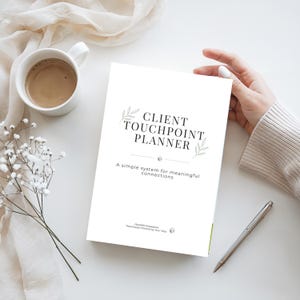 Può includere: Un'agenda bianca intitolata "Client Touchpoint Planner" con decorazioni floreali e il claim "A simple system for meaningful connections". Una tazza di caffè, una penna e dei fiori sono anche sulla superficie bianca.