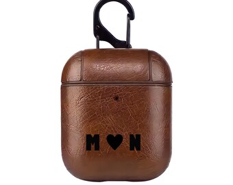 May include: Brown leather Airpods case with a black carabiner clip and the letters "M" and "N" with a heart symbol in between.