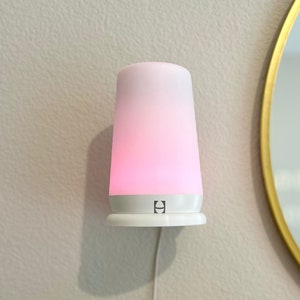 May include: A white Hatch Rest sound machine with a pink light, plugged into an outlet and mounted on a wall. Hatch Rest not included.