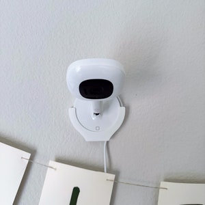May include: A white security camera mounted on a white ceiling mount. The camera has a black lens and a white cord.