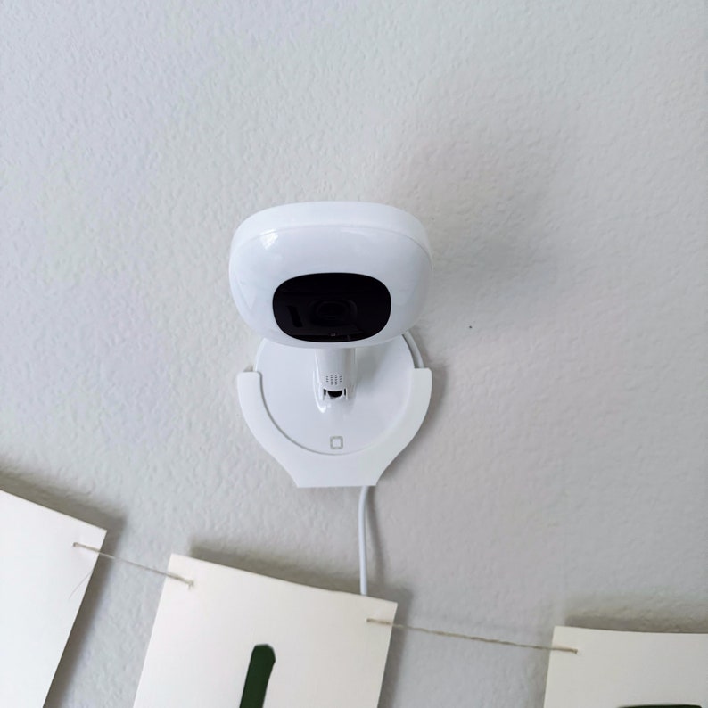 May include: A white security camera mounted on a white ceiling mount. The camera has a black lens and a white cord.