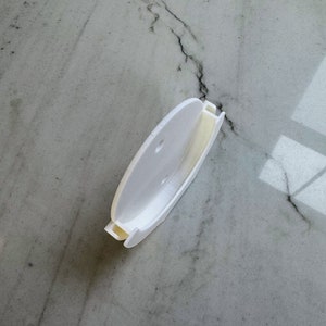 May include: White plastic wall mount with two holes for hanging. The mount is designed to hold a round object, such as a clock or a mirror.