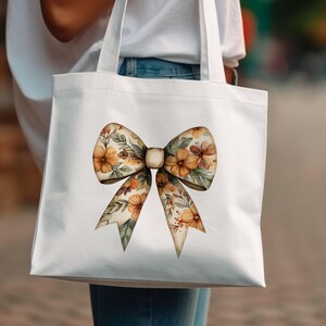 May include: A white tote bag with a floral bow design. The bow is made of watercolor flowers in shades of orange, yellow, and brown.