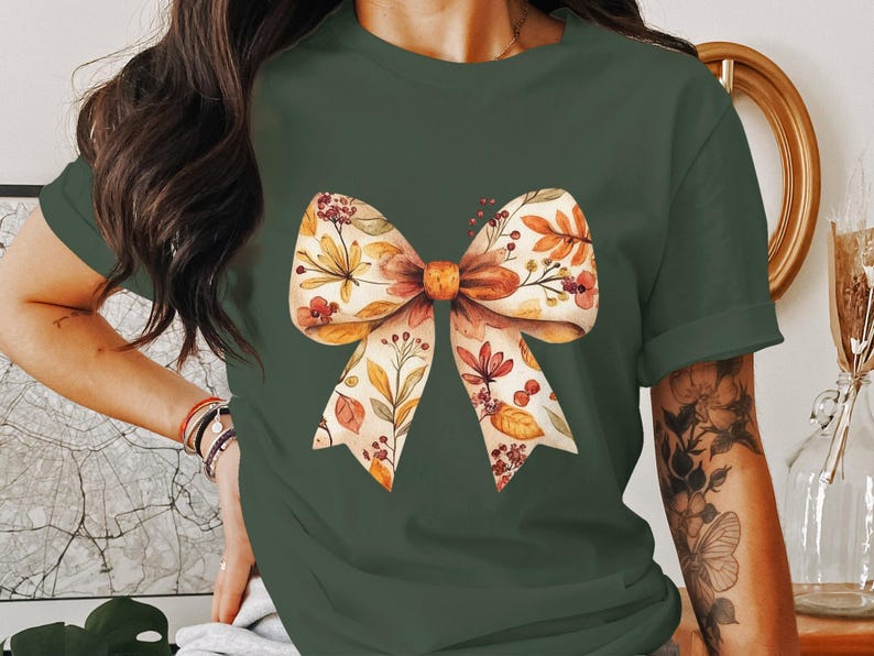May include: A green t-shirt with a floral bow design. The bow is made of white fabric with orange and brown floral accents.