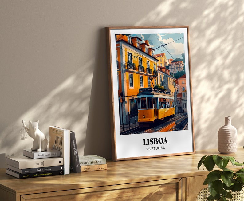 May include: A framed illustration of a yellow tram traveling through a street in Lisbon, Portugal. The illustration features colorful buildings and a blue sky. The text "LISBOA PORTUGAL" is printed below the tram.