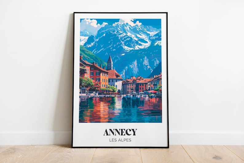 May include: A vintage travel poster featuring a colorful illustration of a town nestled in the French Alps. The poster has the text "Annecy Les Alpes" at the bottom.