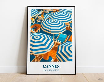 Puede incluir: Una impresión artística enmarcada que presenta una escena de playa con sombrillas a rayas azules y blancas, tumbonas naranjas y el texto "Cannes La Croisette". La obra de arte evoca unas vacaciones soleadas junto al mar.