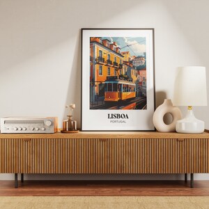 May include: A vintage-style poster with a yellow tram in Lisbon, Portugal. The poster is framed and hanging on a wall above a wooden media console with a stereo receiver and a lamp.