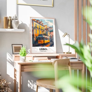 May include: A framed poster with a colorful illustration of a yellow tram in Lisbon, Portugal. The poster is hanging on a white wall above a wooden desk with a chair and a lamp.