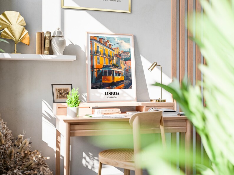 May include: A framed poster with a colorful illustration of a yellow tram in Lisbon, Portugal. The poster is hanging on a white wall above a wooden desk with a chair and a lamp.